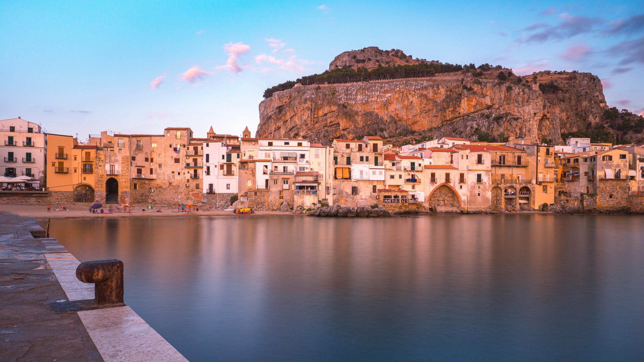 A Sicilian city by water. Beautiful pink clouds line the sky.