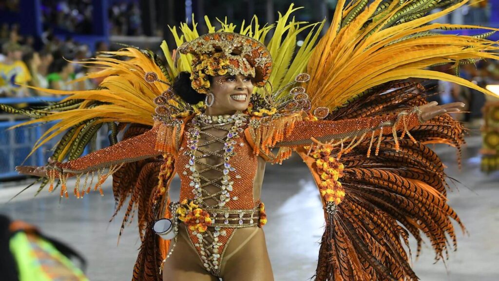 Dancer in vibrant carnival costume with elaborate headdress and feathered wings at a parade, celebrating sustainable tourism in Latin America.