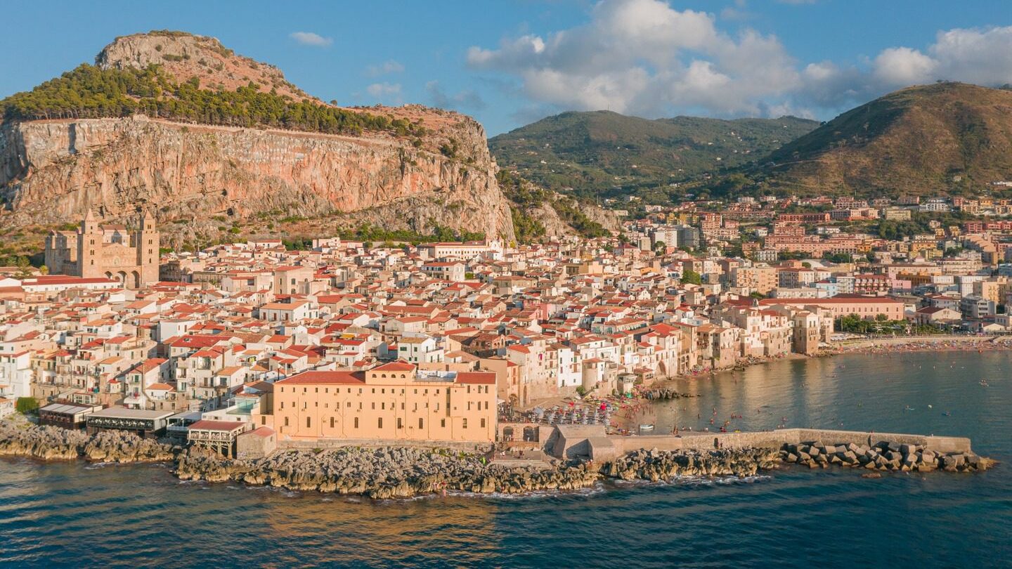 A panoramic view of Sicily with traditional Italian homes and lush green mountains in the background.