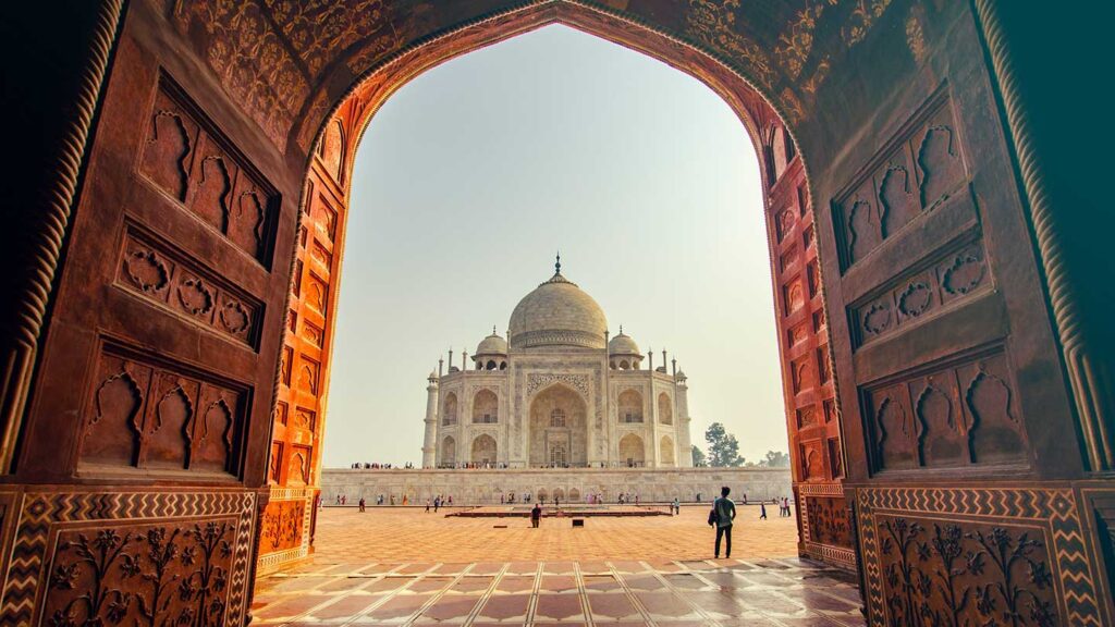 View of the Taj Mahal through an ornate archway, showcasing its white marble domes and a clear blue sky in the background, epitomizing retirement travel goals.