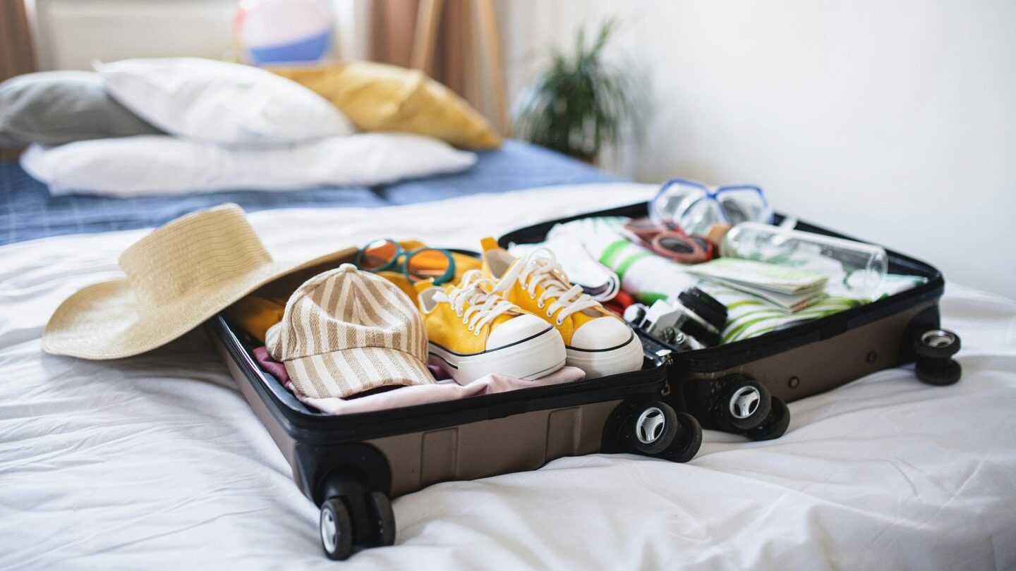 an open suitcase with shoes and clothes inside on a bed