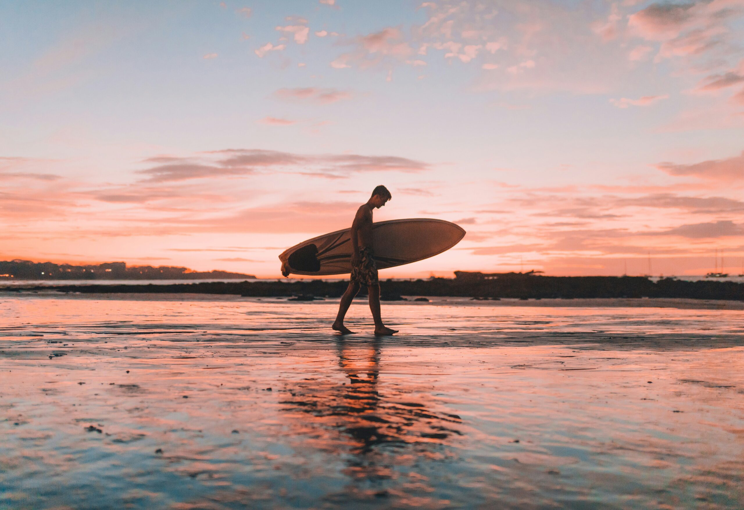 Man with surfboard walks along a beach