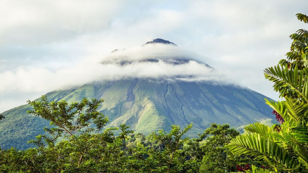 Clouds envelop a volcano visible above the tree tops in Costa Rica