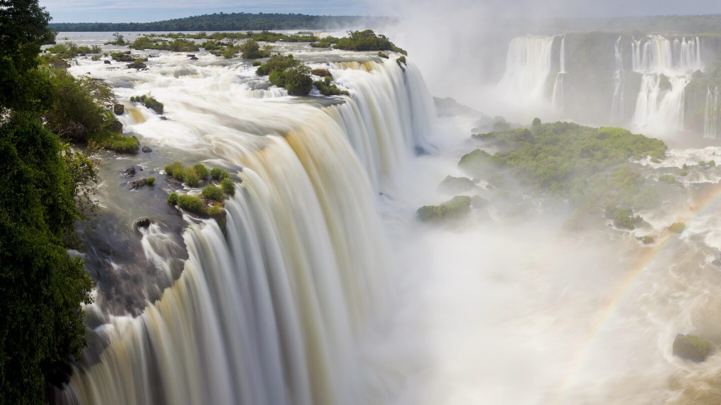 Sweeping view of a cascading waterfall with a rainbow arcing in the mist from my Brazil trip planner.