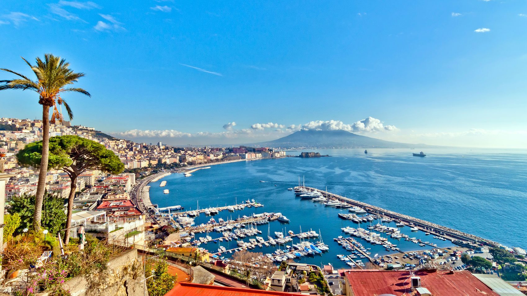 Naples in Italy, buildings lining the left and the sea on the right. Mount Vesuvius is in the background.