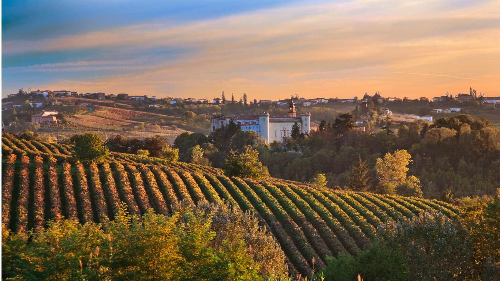 Piedmont in Italy, large villa-like building in the middle with rolling hills in the foreground. At dusk.