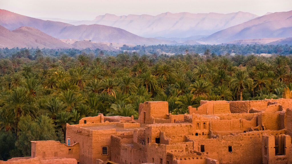 Traditional Berber dwellings with palm trees and distant Atlas Mountains in Morocco