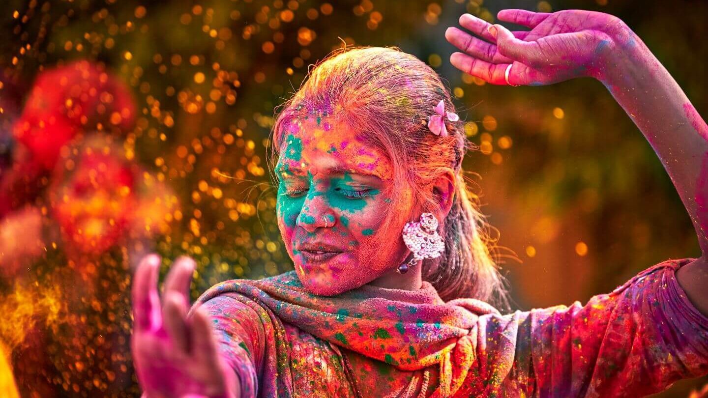 A woman covered in powered paint dancing outside at Holi festival.