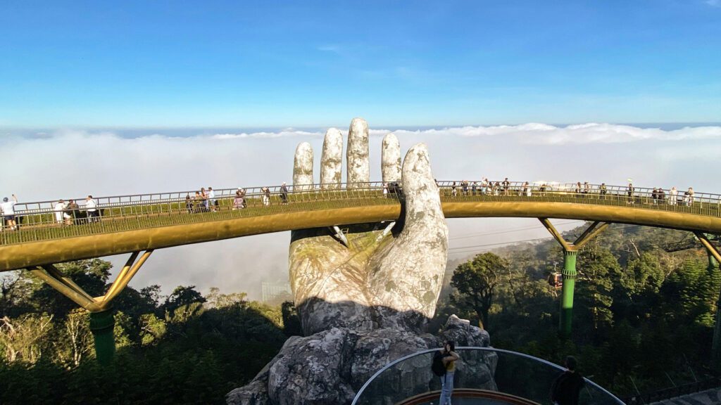 People walking across a bridge supported by a giant concrete hand