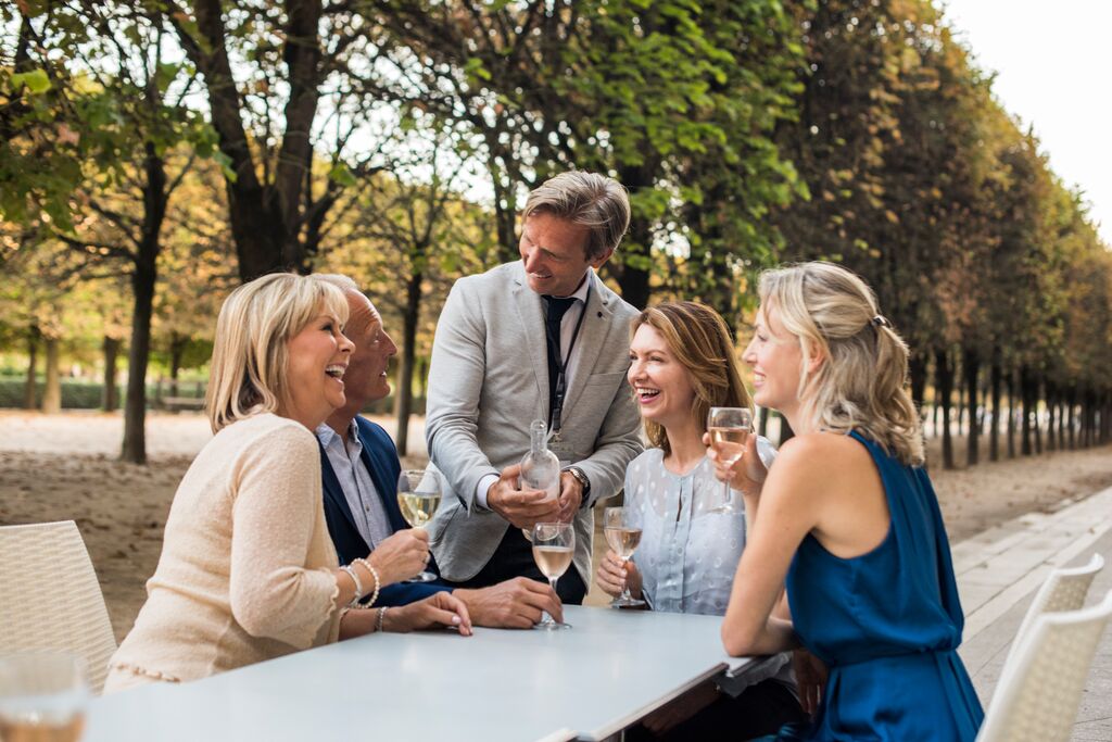 Paris travel director pouring group of four well-dressed guests a drink in a park
