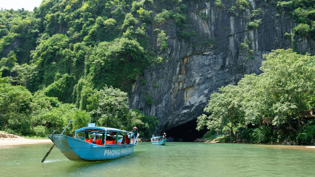 People on a small tourist boat on a river with a cave system in the background