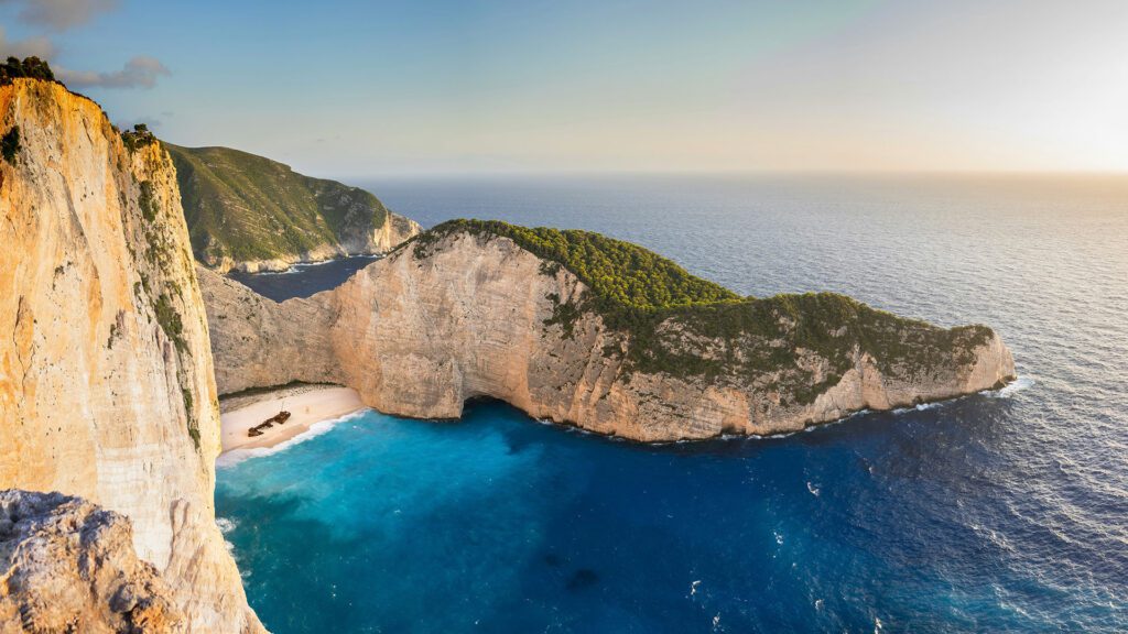 Aerial view of shipwreck beach with turquoise waters, steep cliffs, and a boat near Zakynthos Island, Greece — a top bucket list destination for 2022.