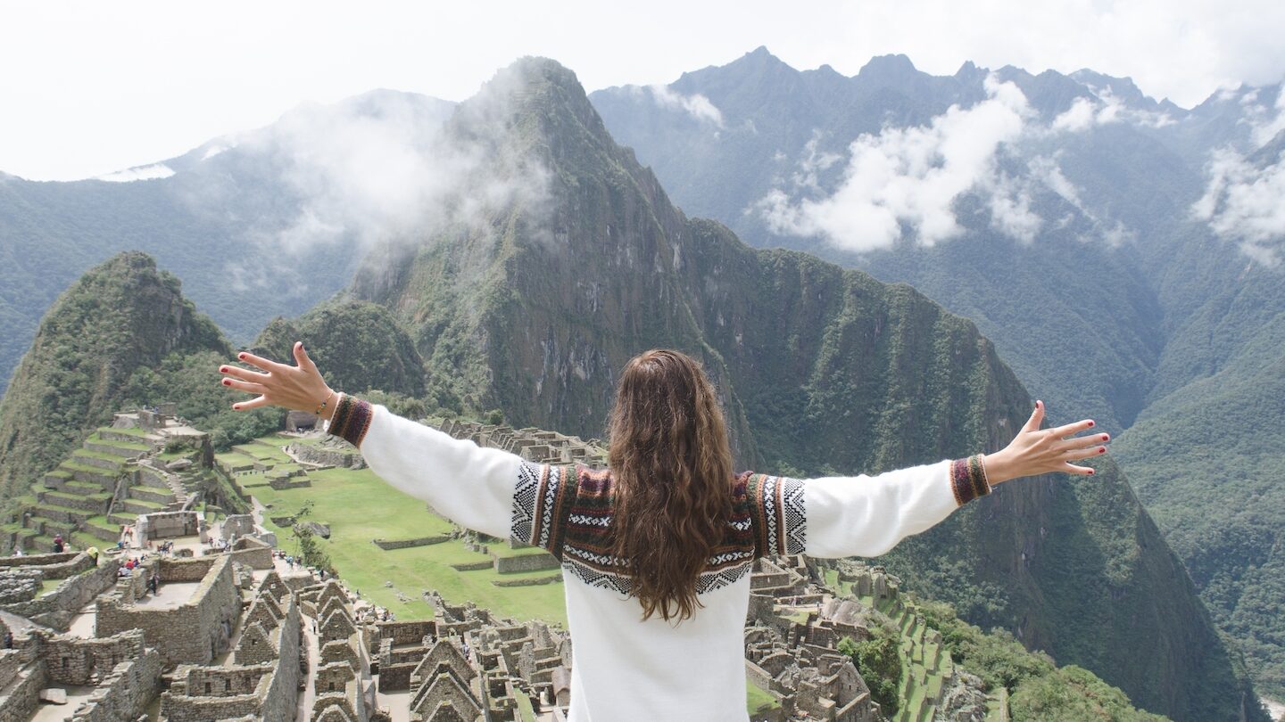 Person with open arms overlooking the ancient inca city of Machu Picchu, enveloped in mist during a tour of Machu Picchu.