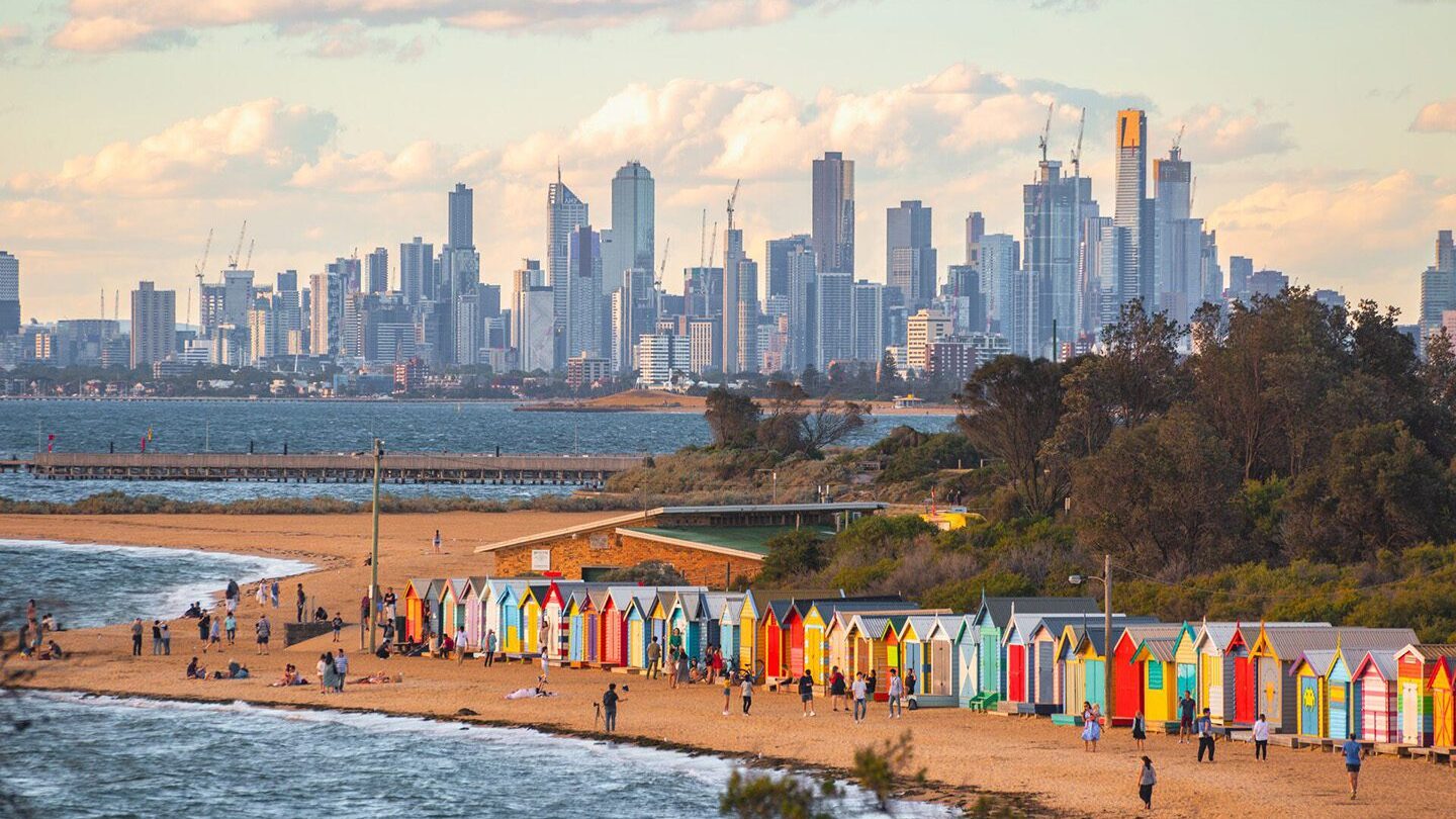 Colorful beach huts on a beach in the foreground, Melbourne city skyline in the distance