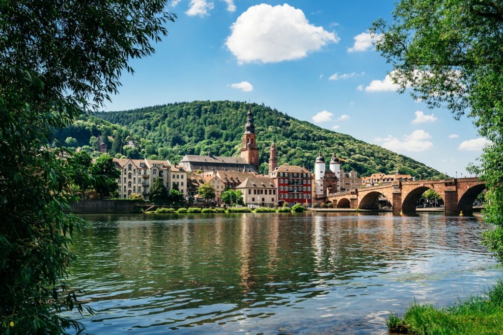 View across the Rhine river of a stone bridge crossing to a cluster of buildings, old Germanic style architecture