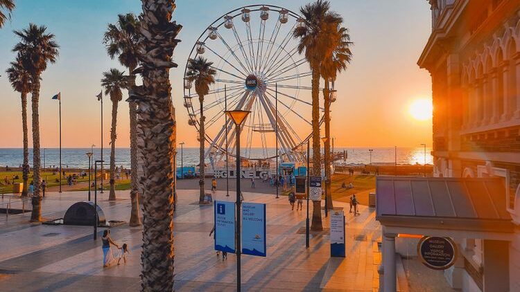 A large ferris wheel dominates the Glenelg Beach horizon during sunset in Adelaide.