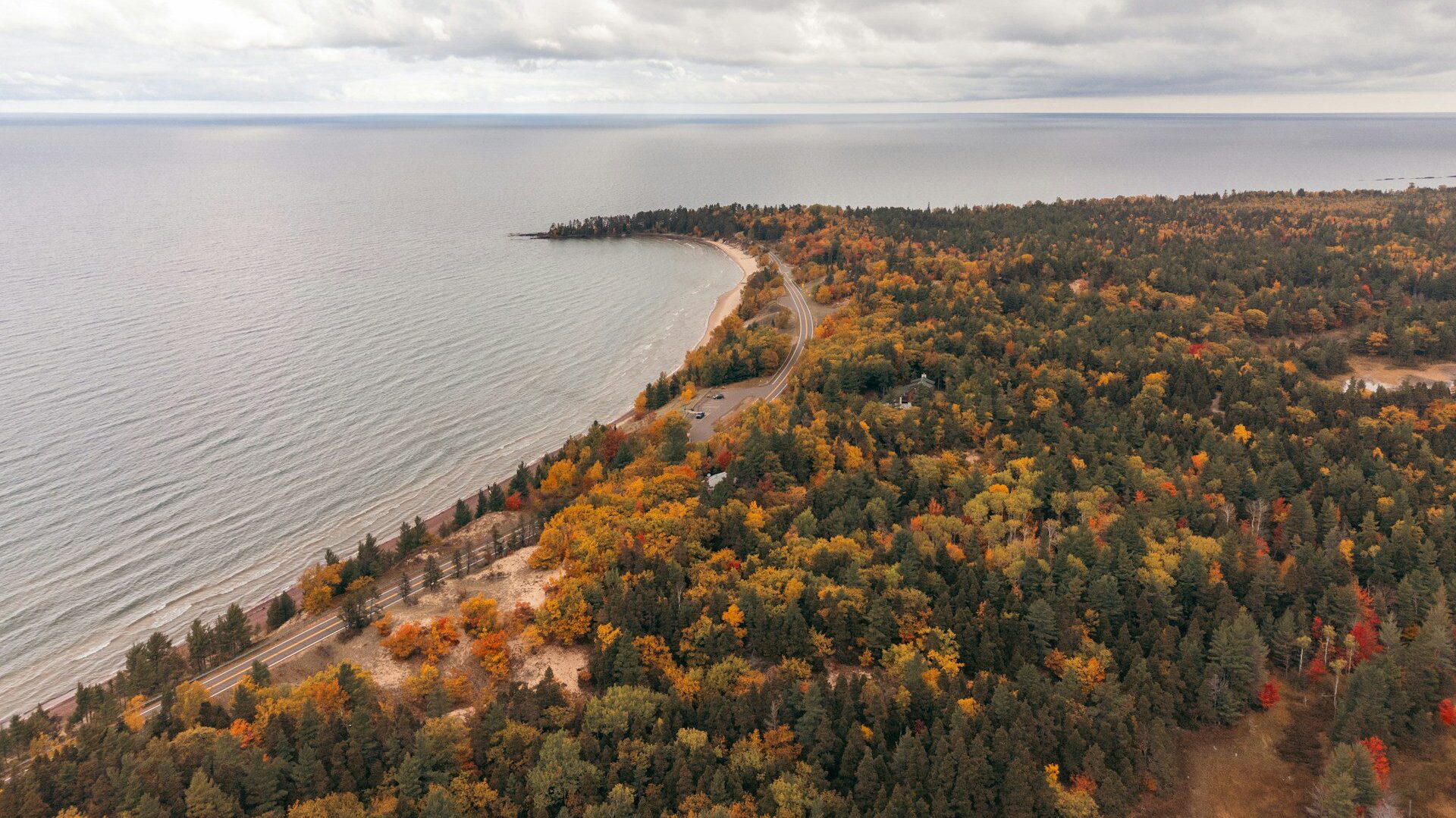 Aerial view of a road running alongside a lake with autumnal trees on one side