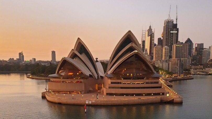 Sunset view of the Sydney Opera House, a popular film location, with the city skyline in the background, reflecting golden hues on the water.