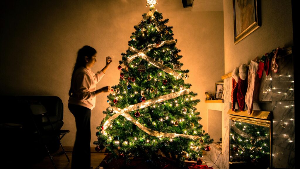 Someone hanging decorations on a Christmas tree with stockings above a fireplace