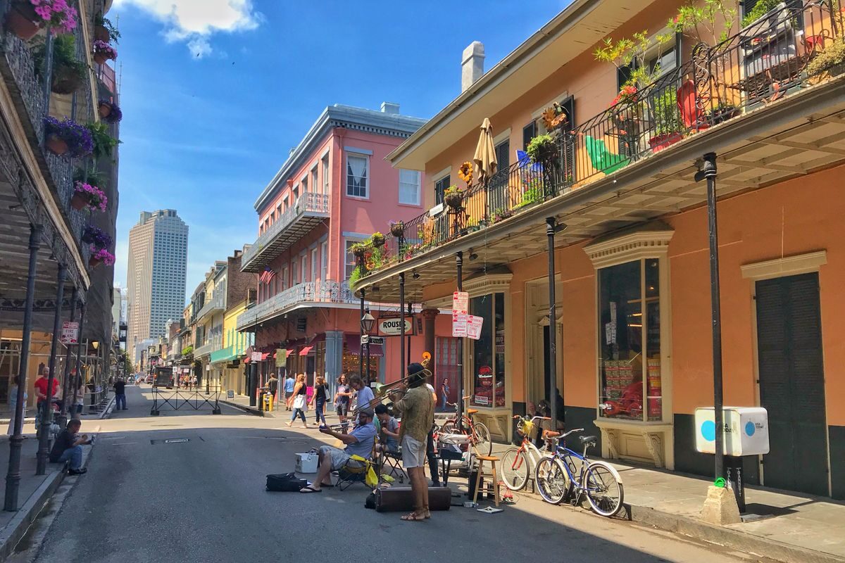 Sunny day on a lively street in New Orleans with pedestrians, cyclists, and a street performer playing drums, showcasing what to do in New Orleans.