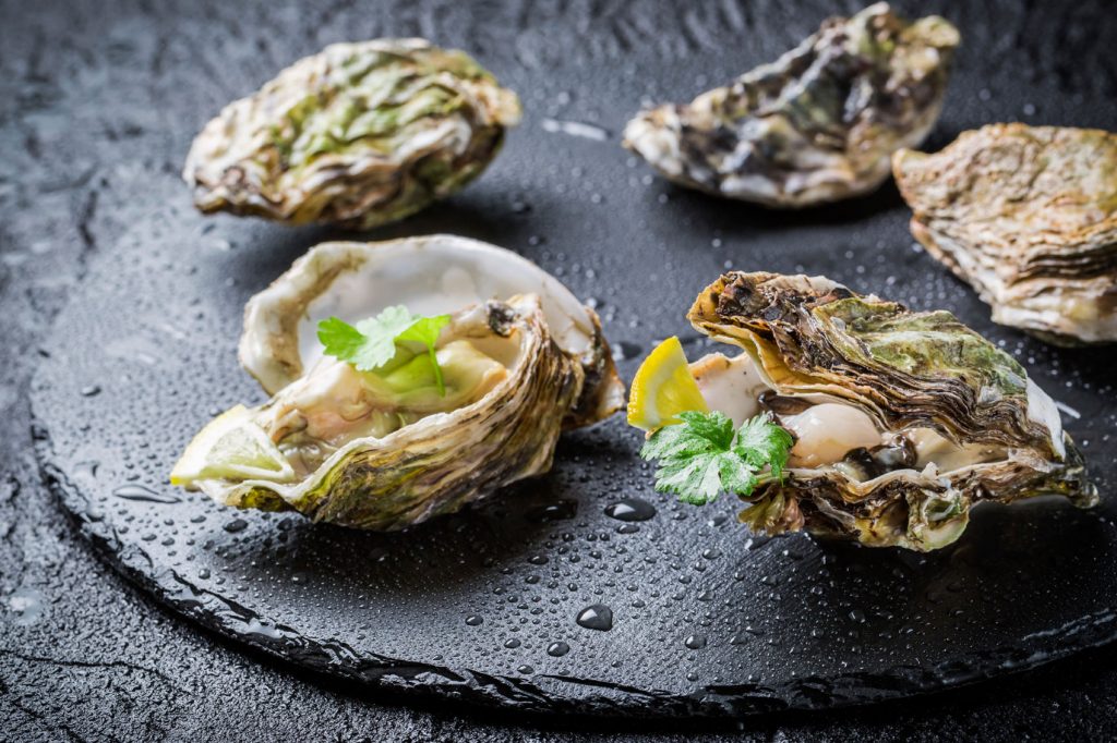 Seasonal British oysters with lemon and parsley on a black plate.