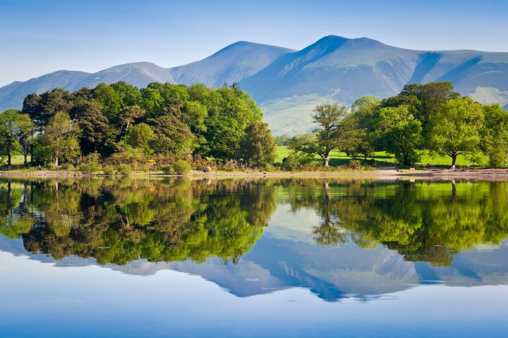 Peaceful image of the Lake Disctrict with trees and mountains reflected in a mirror lake