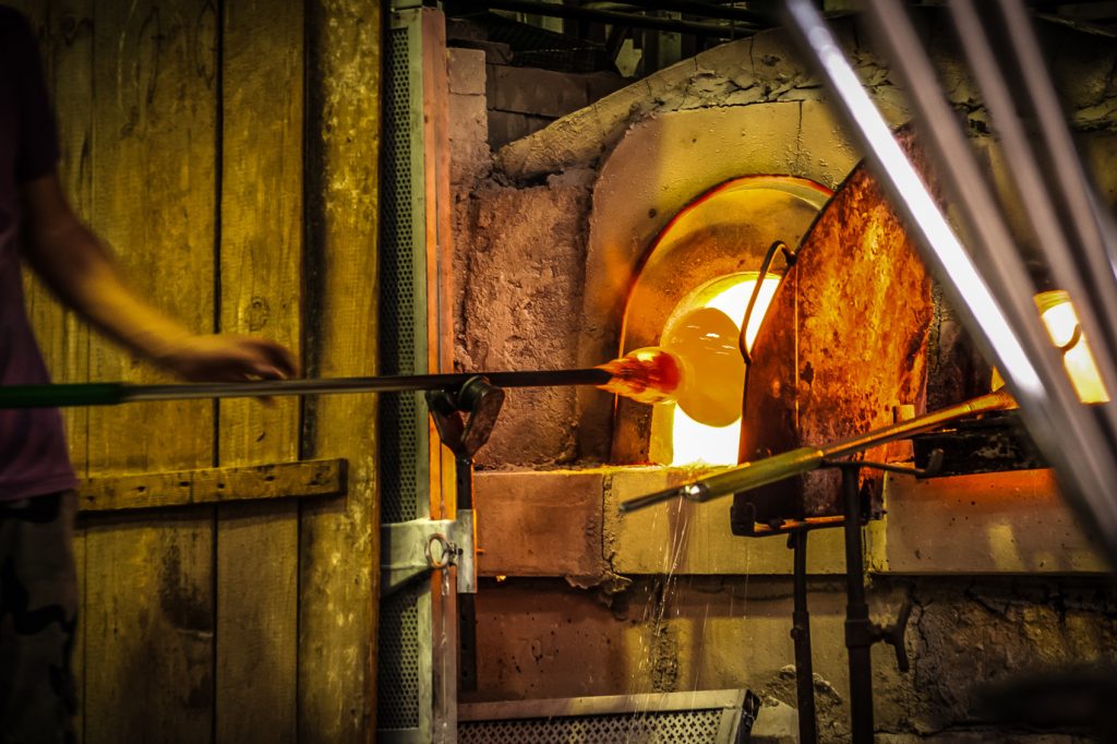 A man is blowing glass in a glass furnace in Venice, providing an insider's view of the city's traditional craft.
