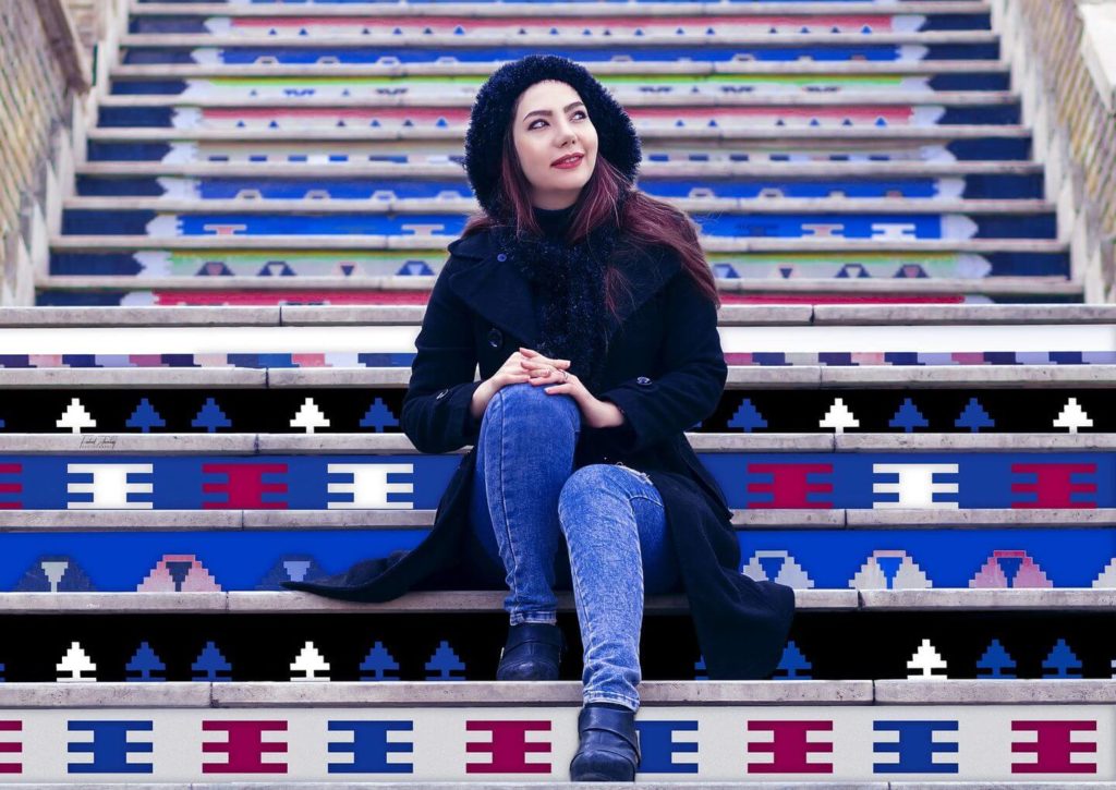 A woman in a black coat and hat sits on colorful patterned steps while looking to her side, exemplifying what to wear in Africa.