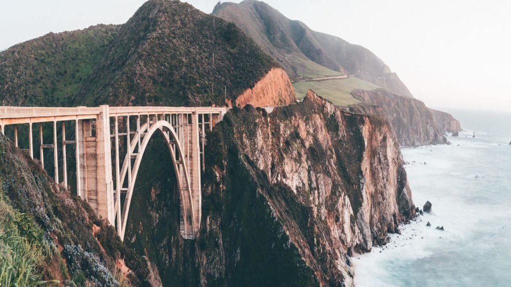 Historic bridge spanning a rugged coastal cliff at sunset in Big Sur, California.