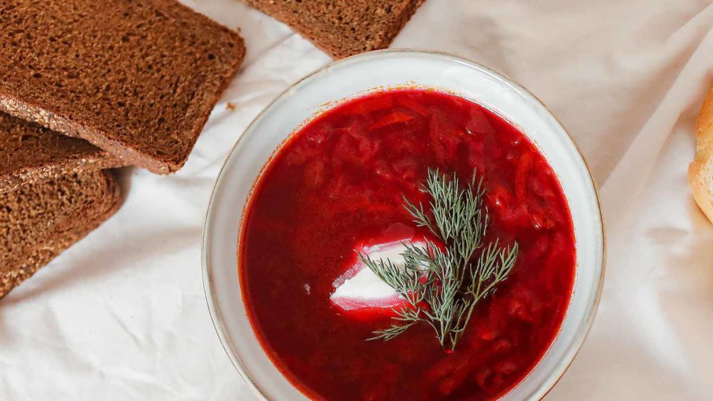 Bowl of borscht garnished with dill, accompanied by slices of brown bread, a staple during Orthodox Christmas traditions.