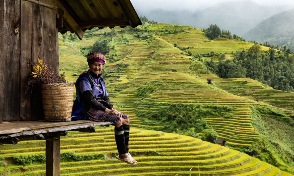 A smiling person in traditional attire sitting on a wooden ledge with terraced fields in the background during the February half term holidays.