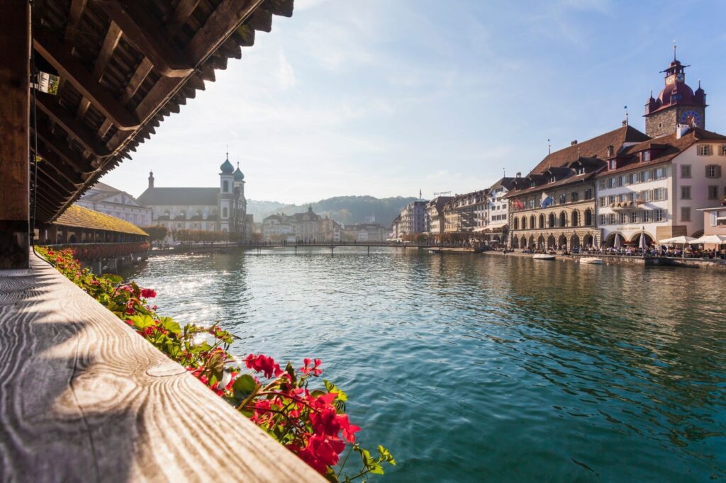 River view in a Swiss city with historic buildings and a bridge with flowers along the railing.