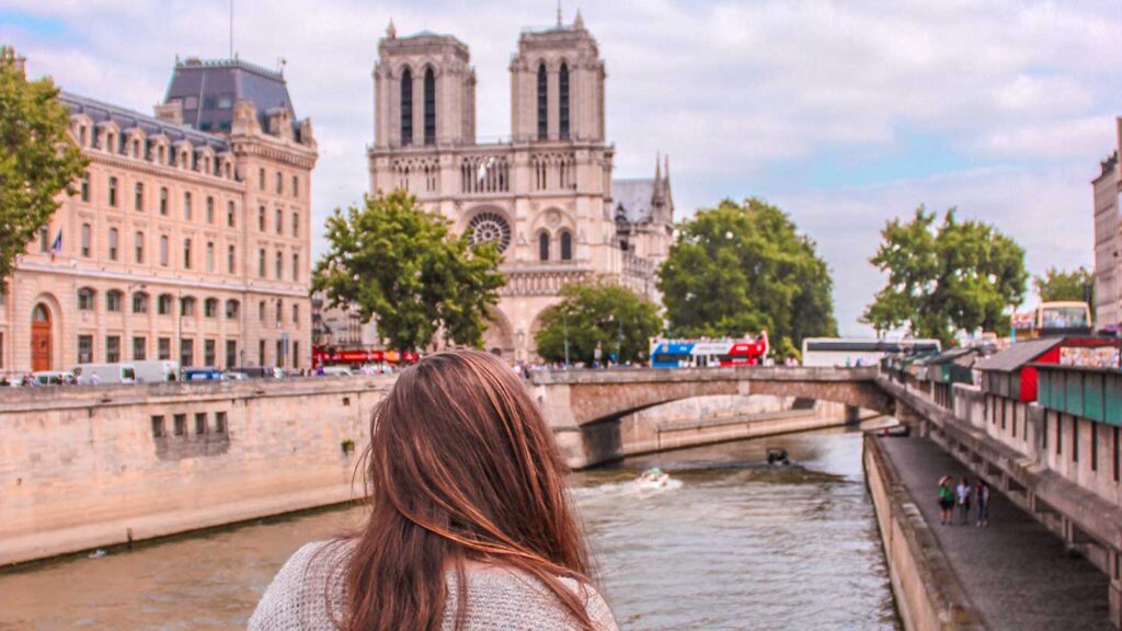 Woman on a solo travel adventure looking at Notre-Dame Cathedral from a bridge over the Seine River in Paris.