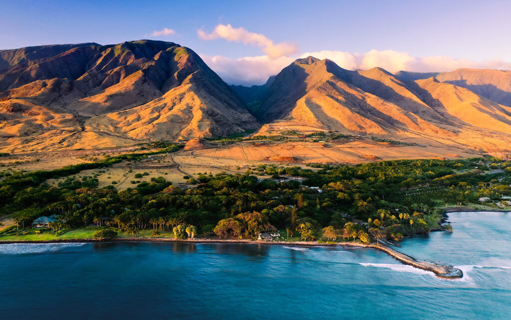 Aerial view of a coastal area at sunset with mountains in the background, featuring a lush green landscape and a clear blue ocean, perfect for adventure family travel.
