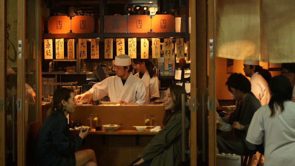 Chef and staff working inside a Japanese restaurant while customers dine and discuss what to eat in Japan at the counter.