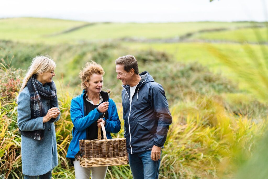 Three people in the countryside, one carrying wicker foraging basket