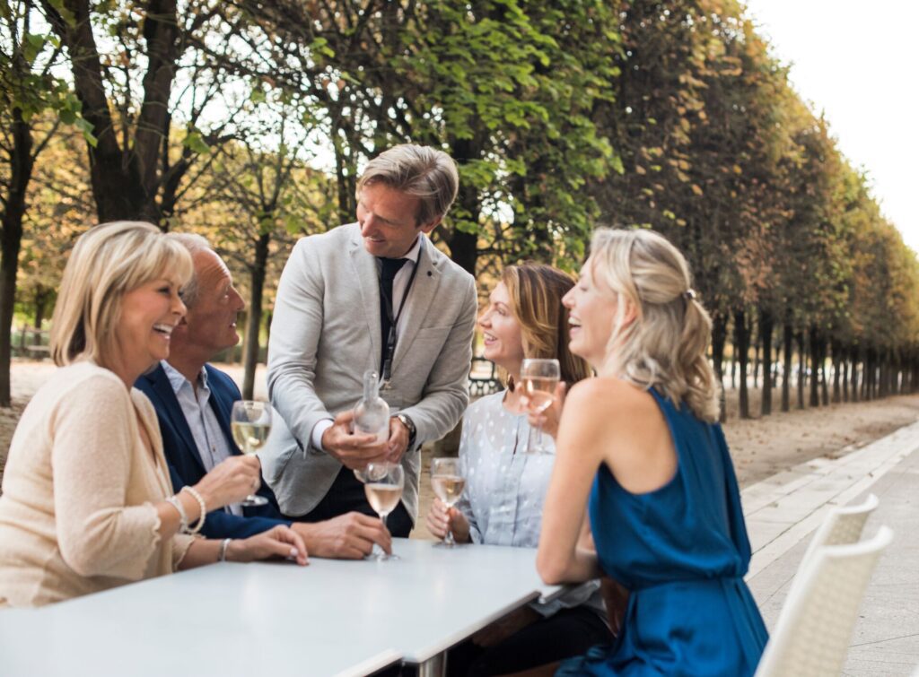A man serving wine to a table of guests who are laughing and smiling
