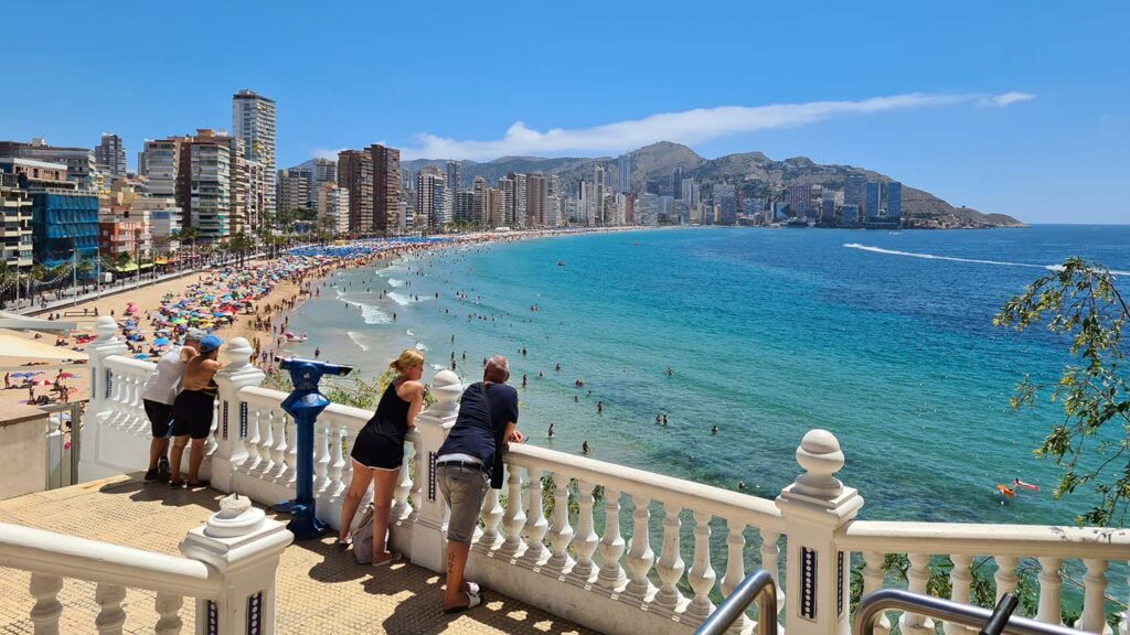 People standing at a viewpoint overlooking a beach in Spain