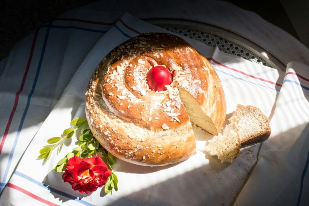 Loaf of bread with a red painted egg in the centre on a tablecloth in the sunlight