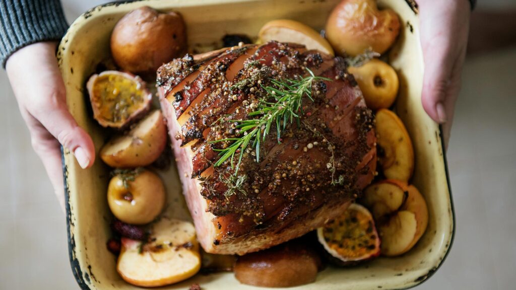 top-down view of hands holding out a roasting dish cooked glazed ham