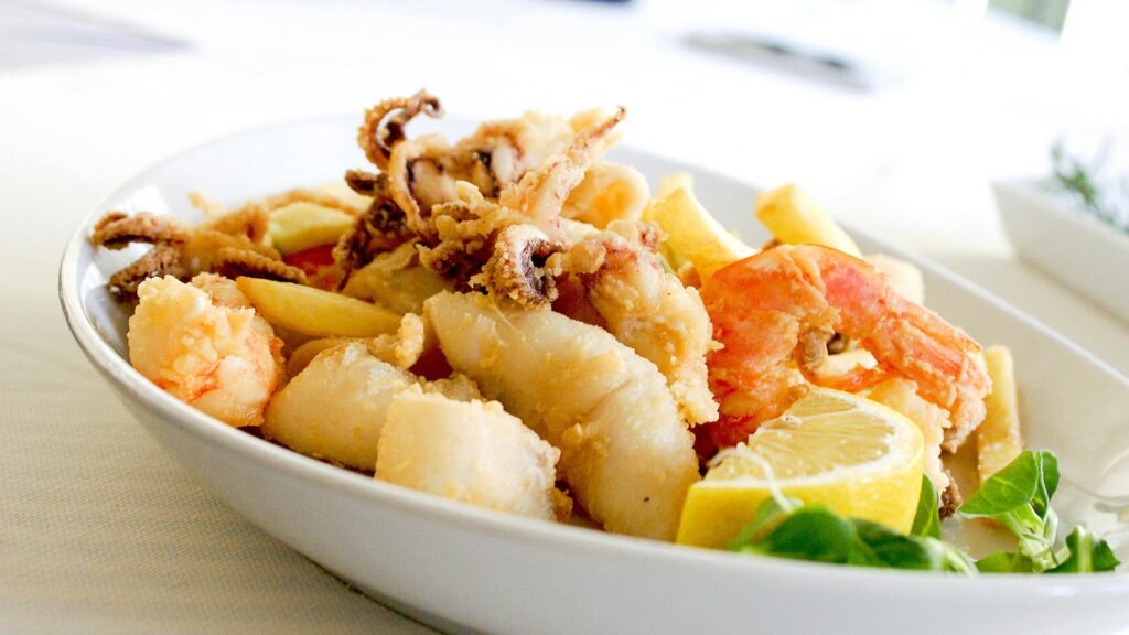 A white bowl filled with lightly fried squid, prawns and pieces of fish.