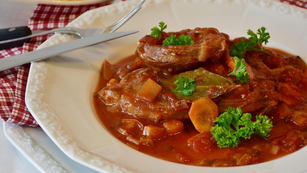 Slow cooked osso buco meat in a white bowl with cutlery and a red checkered napkin