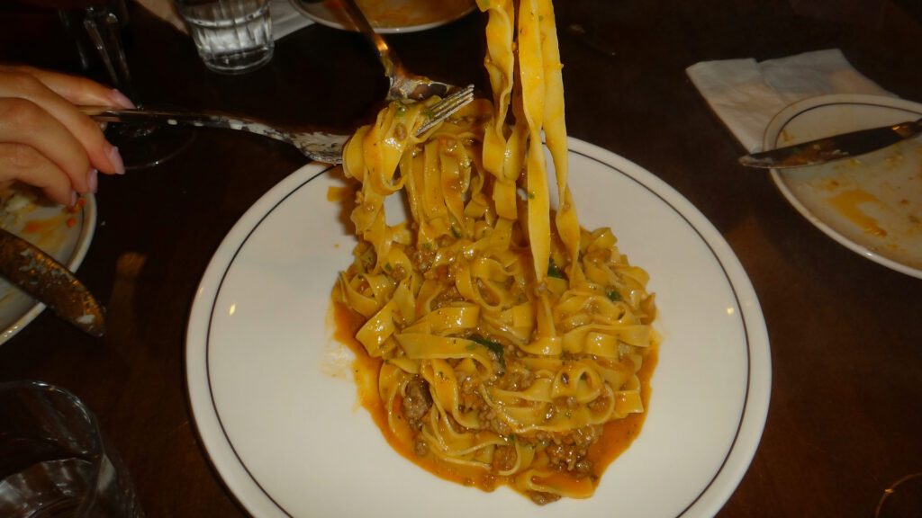 Three hands reaching into a bowl of ragu with forks