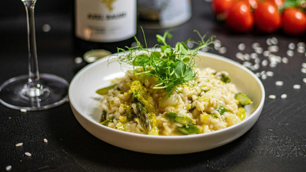 A while bowl filled with Risotto agli Asparagi (Spring asparagus risotto) with pea shoots on top