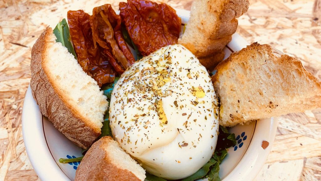 Burrata at the center of a white Puglian bowl with sundried tomatoes and sliced bread