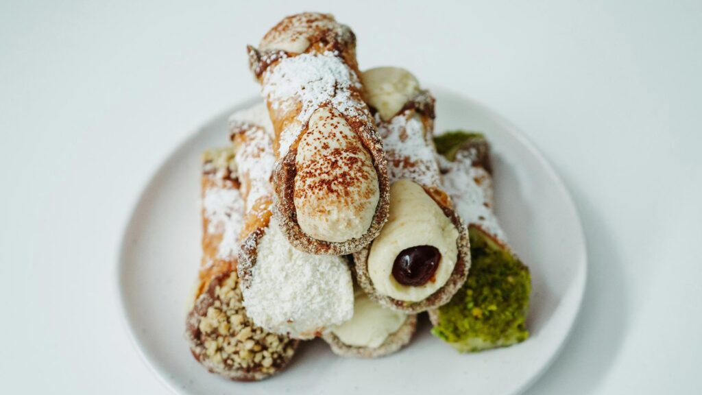 A triangular stack of six cannoli with different fillings, dusted with icing sugar