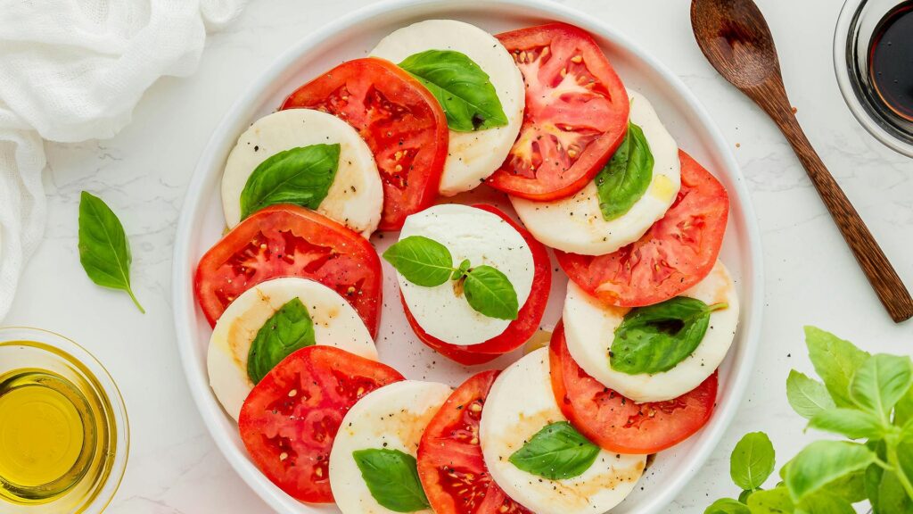A Caprese salad shoot from above showing a swirl of tomato and mozzarella cheese with basil