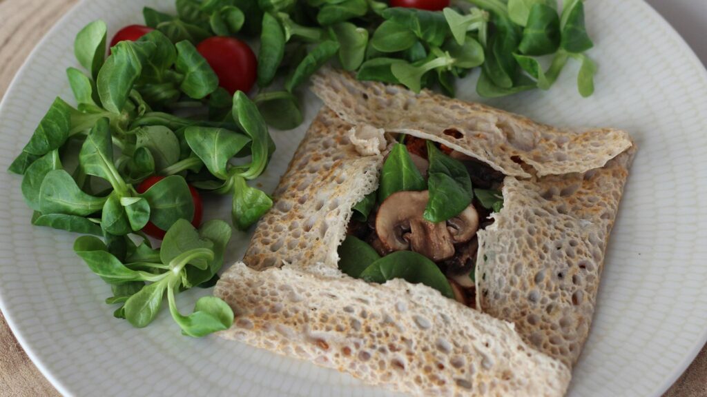 A buckwheat galette with a watercress salad on a white plate