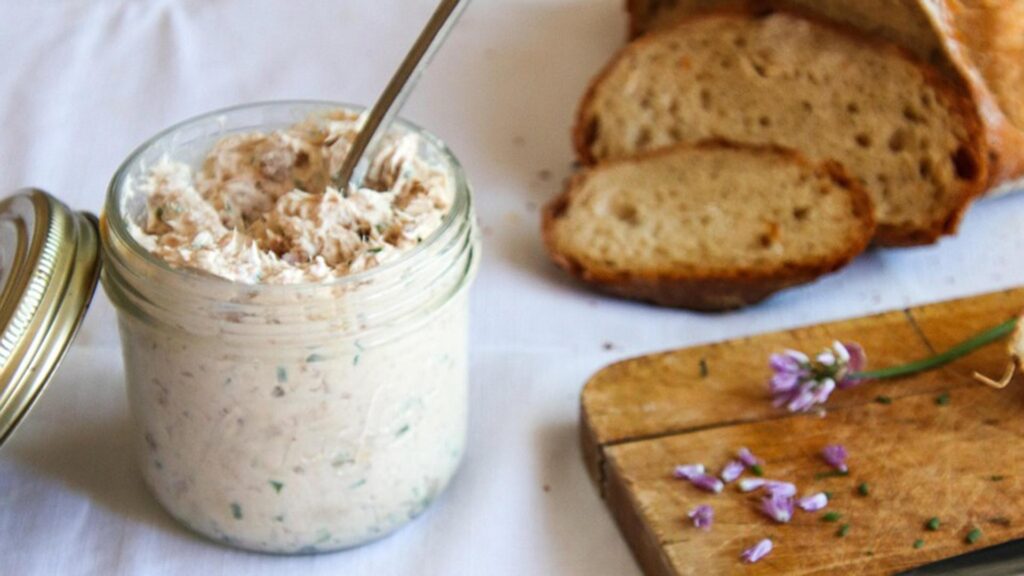 A jar filled with Rillettes de Porc, a pork meat paste with bread slices in the background