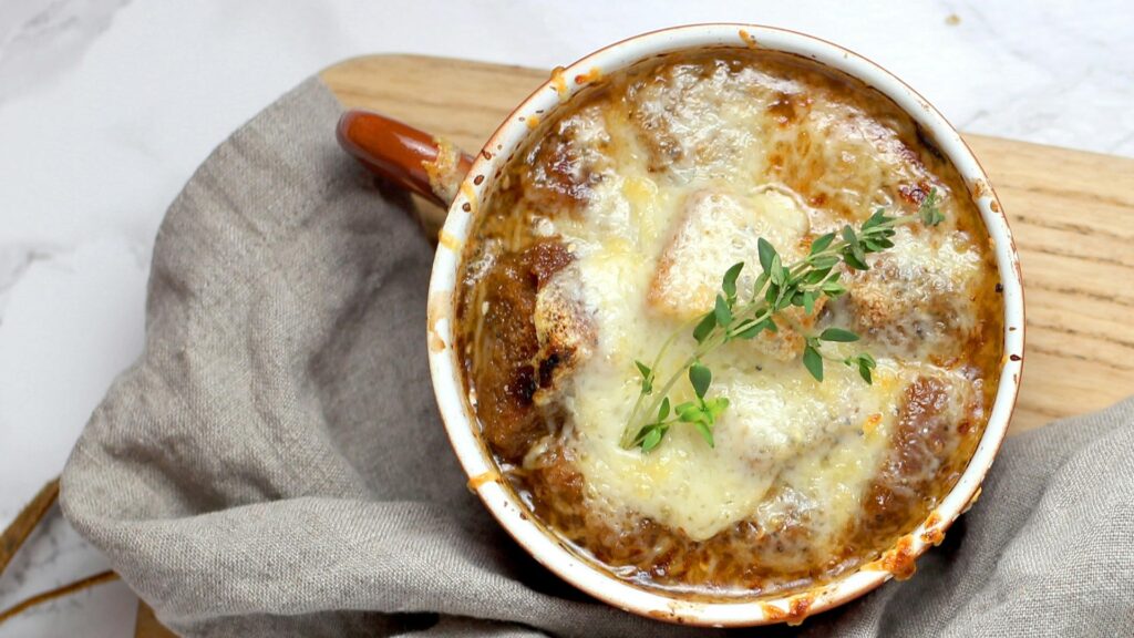 A large mug of French onion soup a gratin with gruyere cheese on top